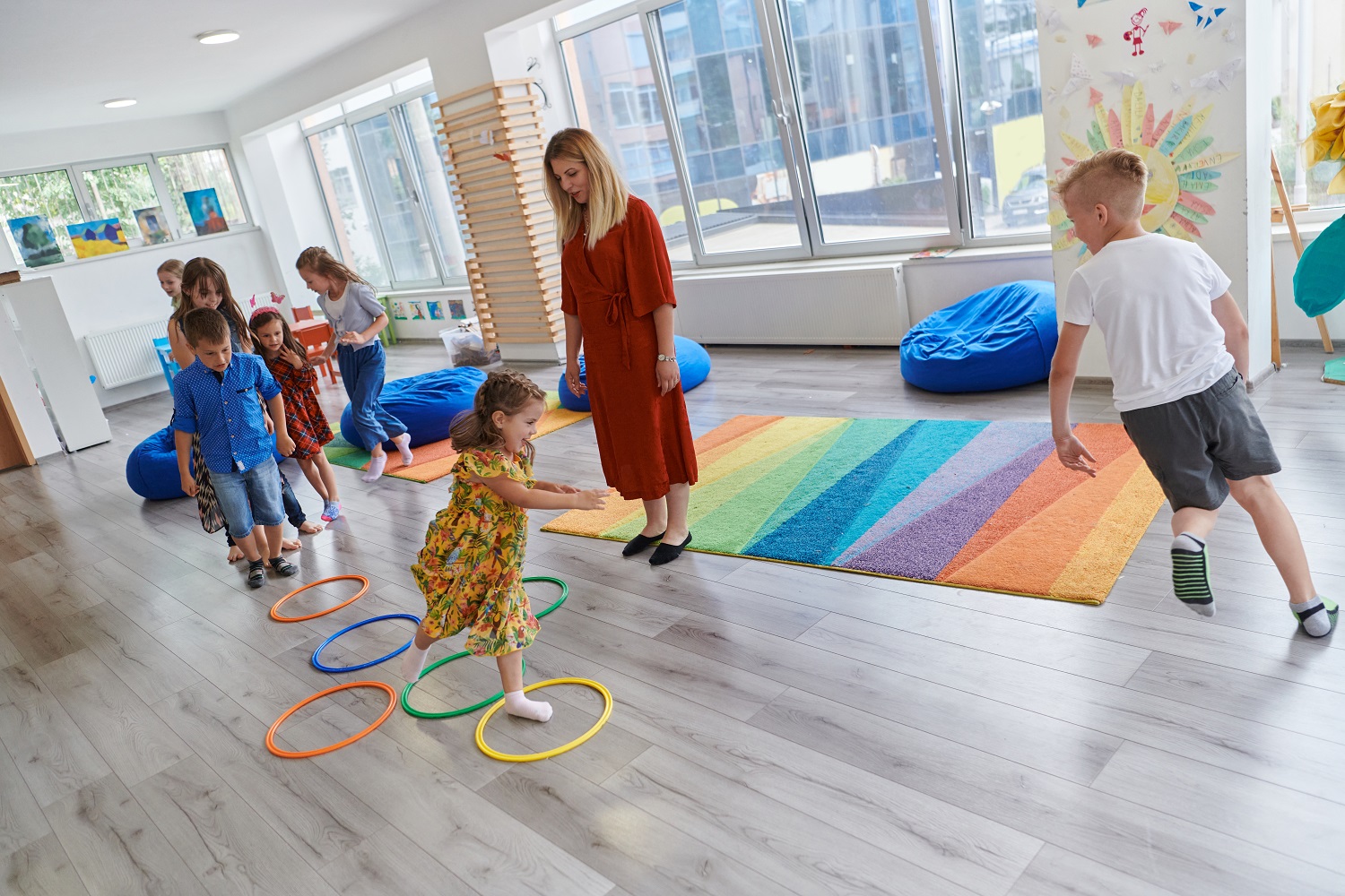 Eine Kindergruppe turnt in einem Raum, eine Erzieherin steht dabei und beobachtet die Situation