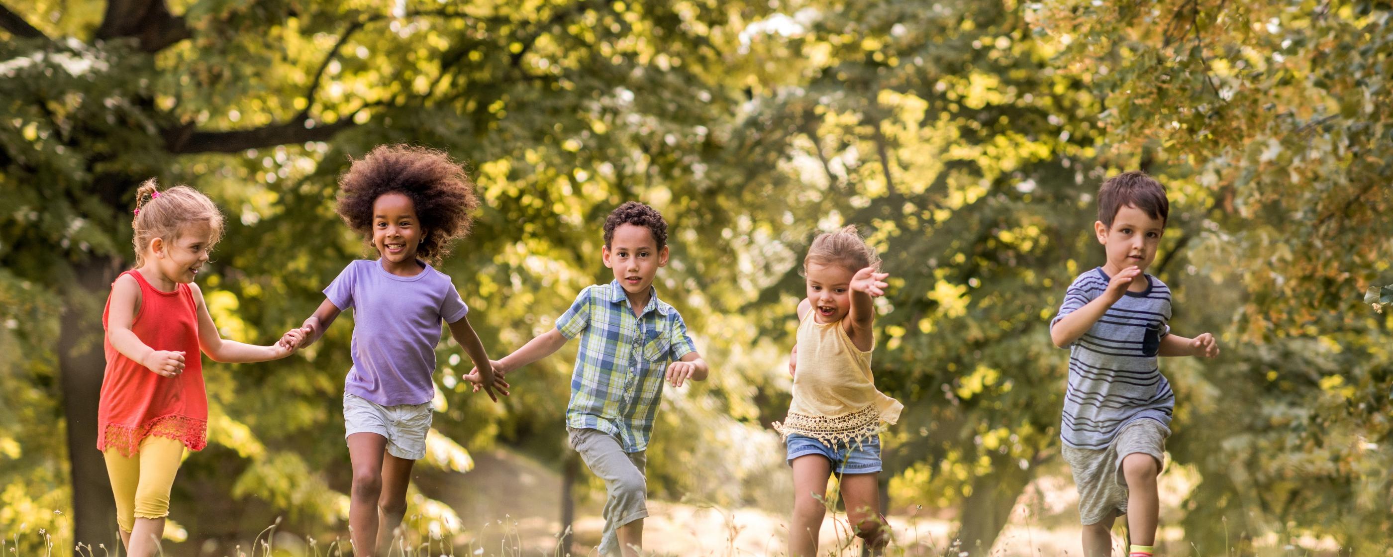 Man sieht lachende Kinder, die über eine Wiese laufen und sich dabei an den Händen halten