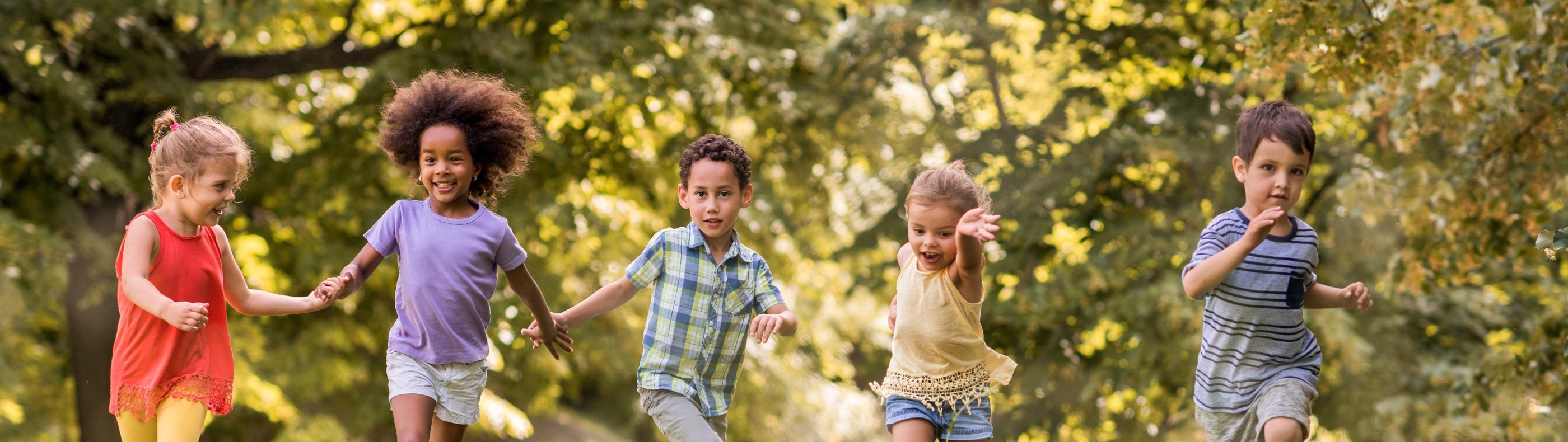 Man sieht lachende Kinder, die über eine Wiese laufen und sich dabei an den Händen halten