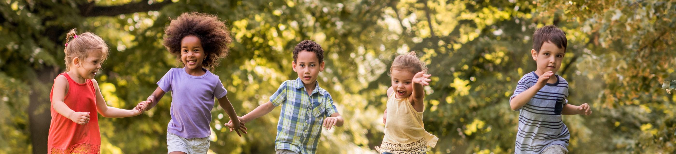 Man sieht lachende Kinder, die über eine Wiese laufen und sich dabei an den Händen halten