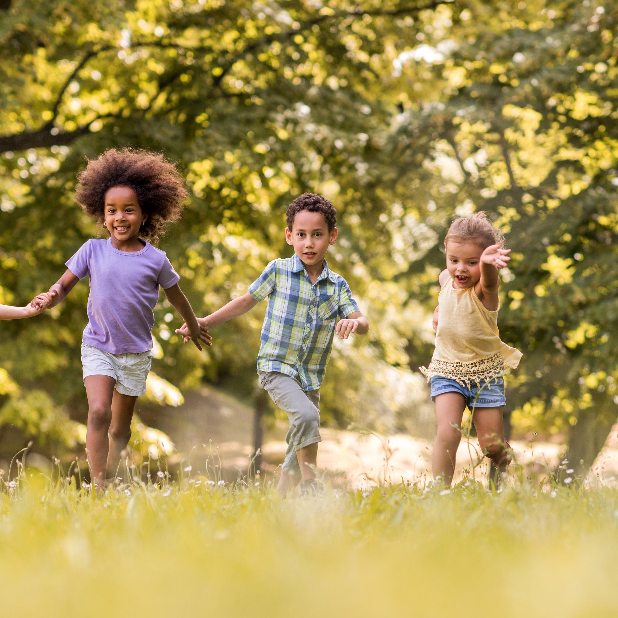 Man sieht lachende Kinder, die über eine Wiese laufen und sich dabei an den Händen halten