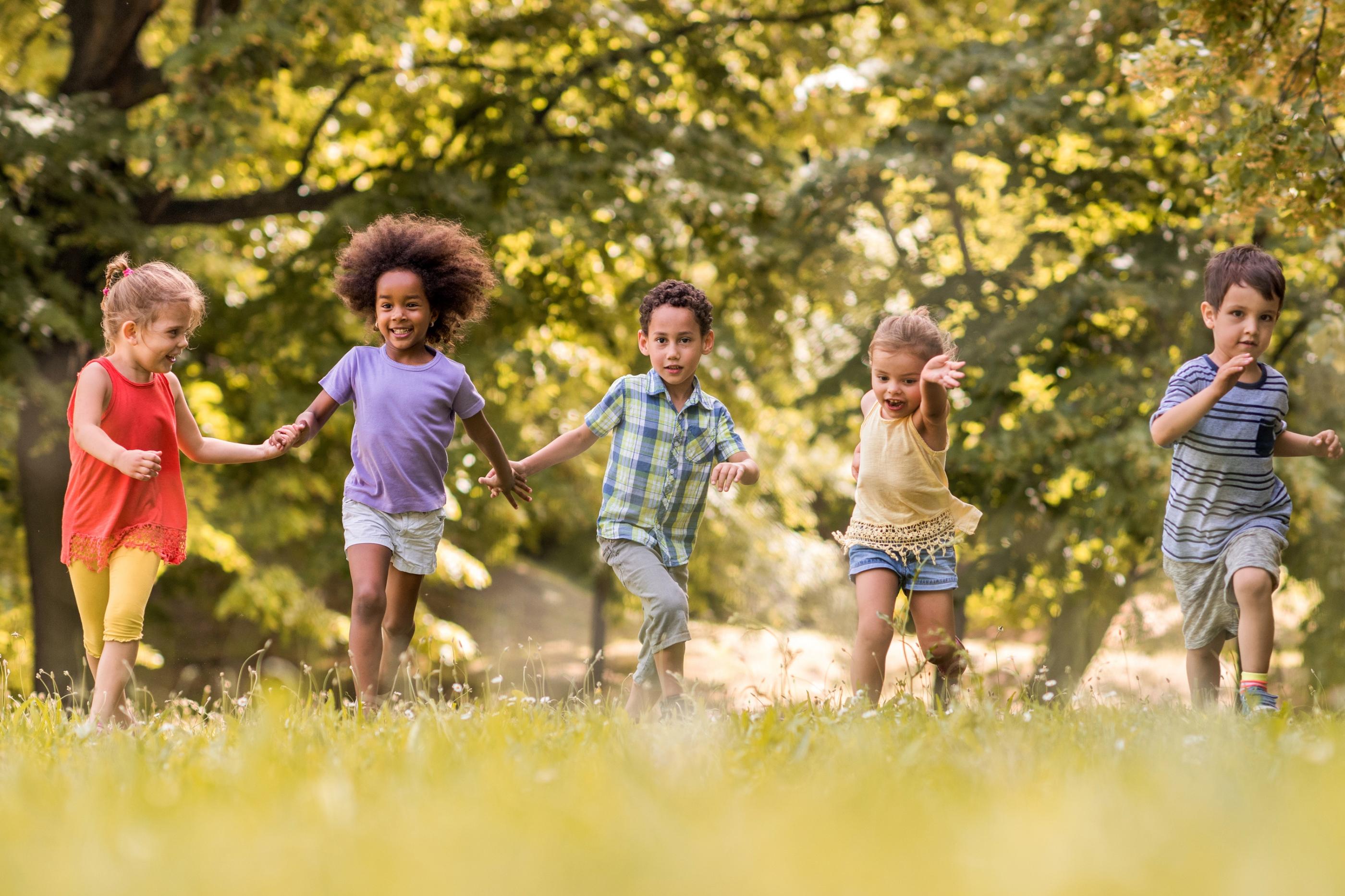 Man sieht lachende Kinder, die über eine Wiese laufen und sich dabei an den Händen halten