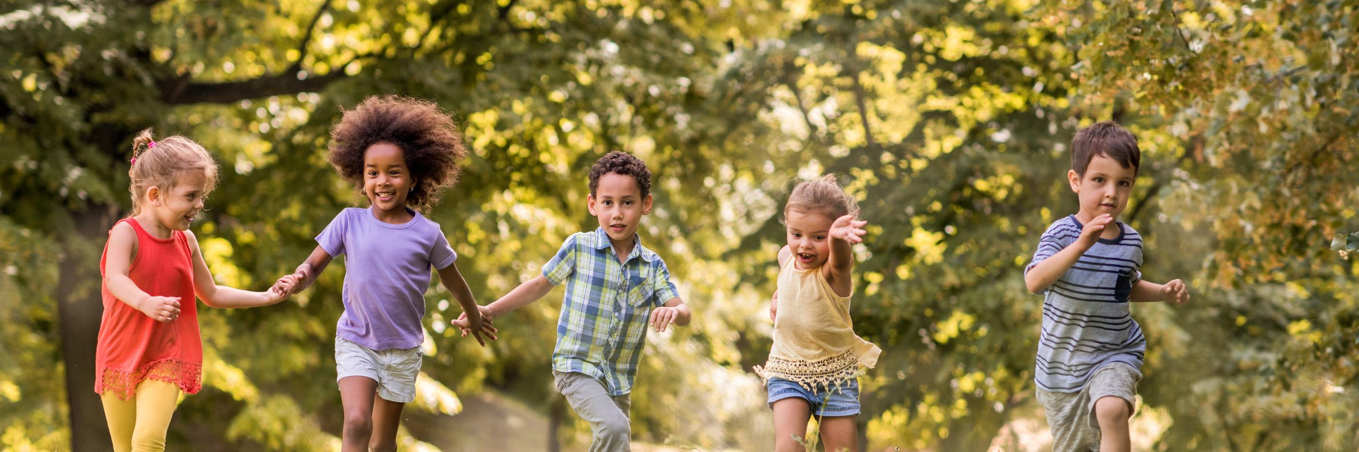 Man sieht lachende Kinder, die über eine Wiese laufen und sich dabei an den Händen halten