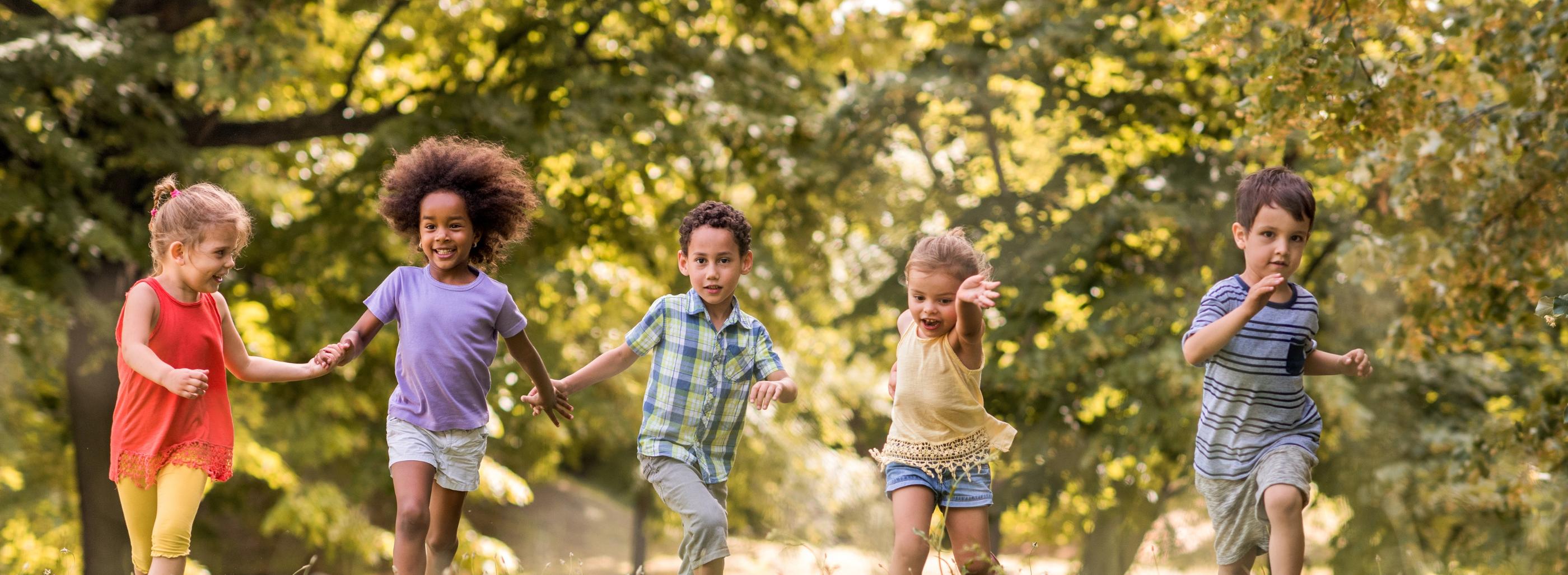 Man sieht lachende Kinder, die über eine Wiese laufen und sich dabei an den Händen halten