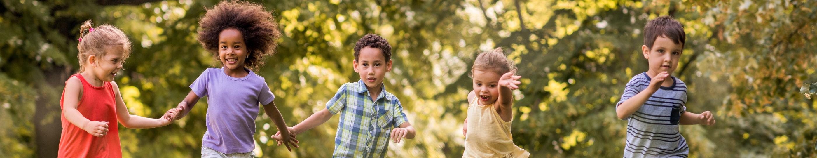 Man sieht lachende Kinder, die über eine Wiese laufen und sich dabei an den Händen halten