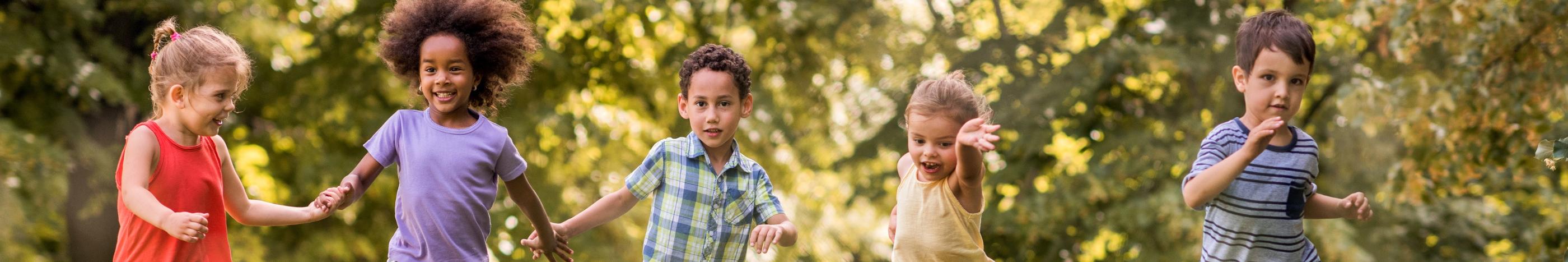 Man sieht lachende Kinder, die über eine Wiese laufen und sich dabei an den Händen halten