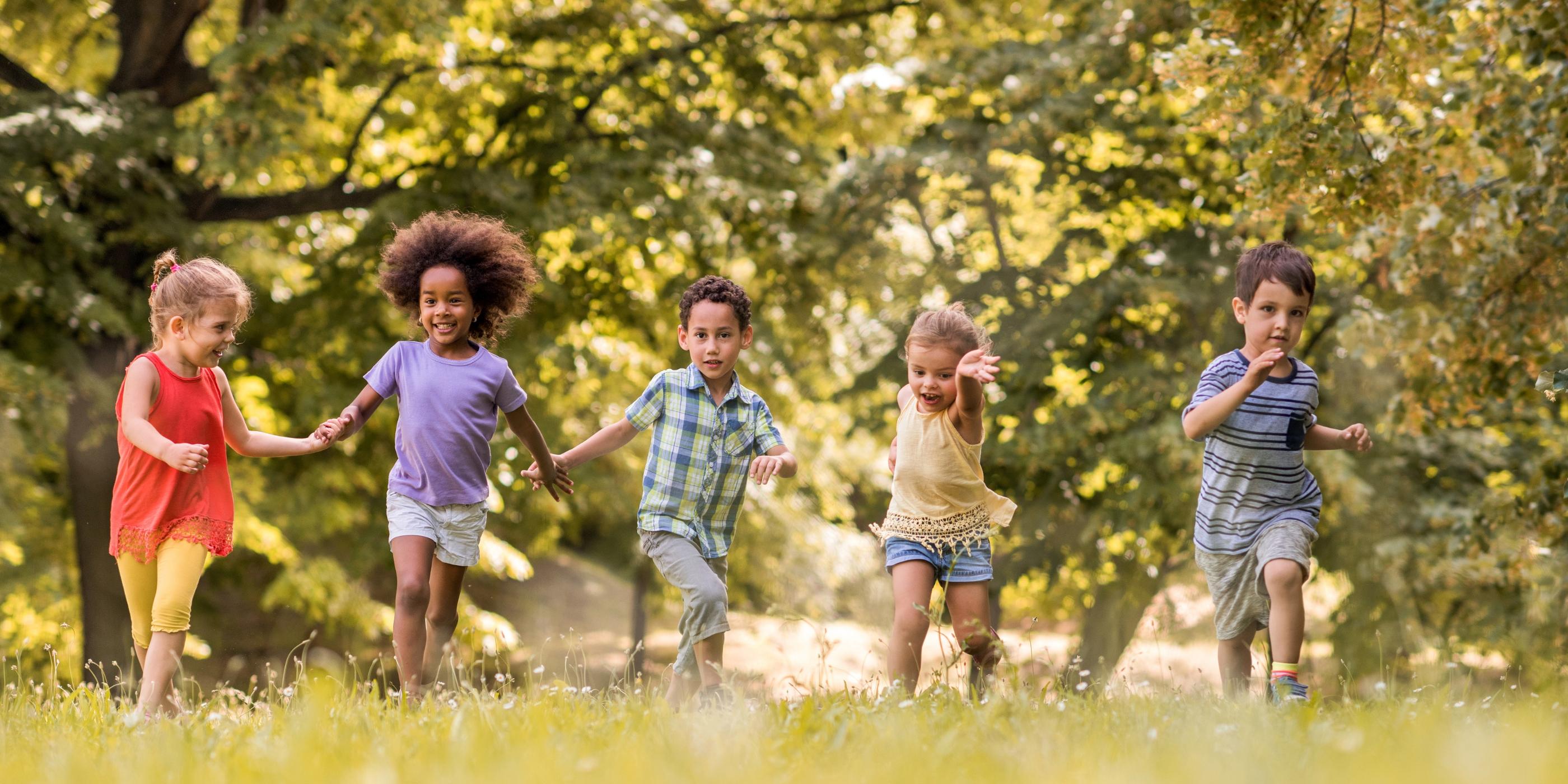 Man sieht lachende Kinder, die über eine Wiese laufen und sich dabei an den Händen halten